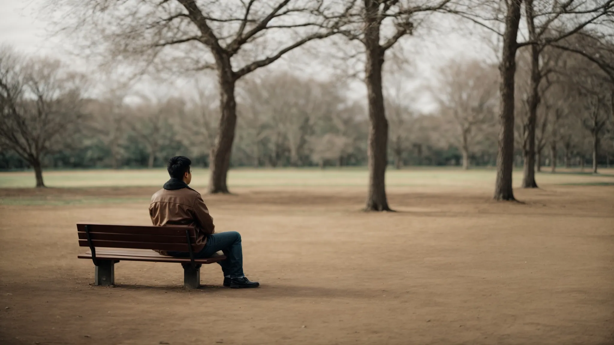 a solitary person sits quietly on a bench in a vast, empty park, contemplating the surrounding space.