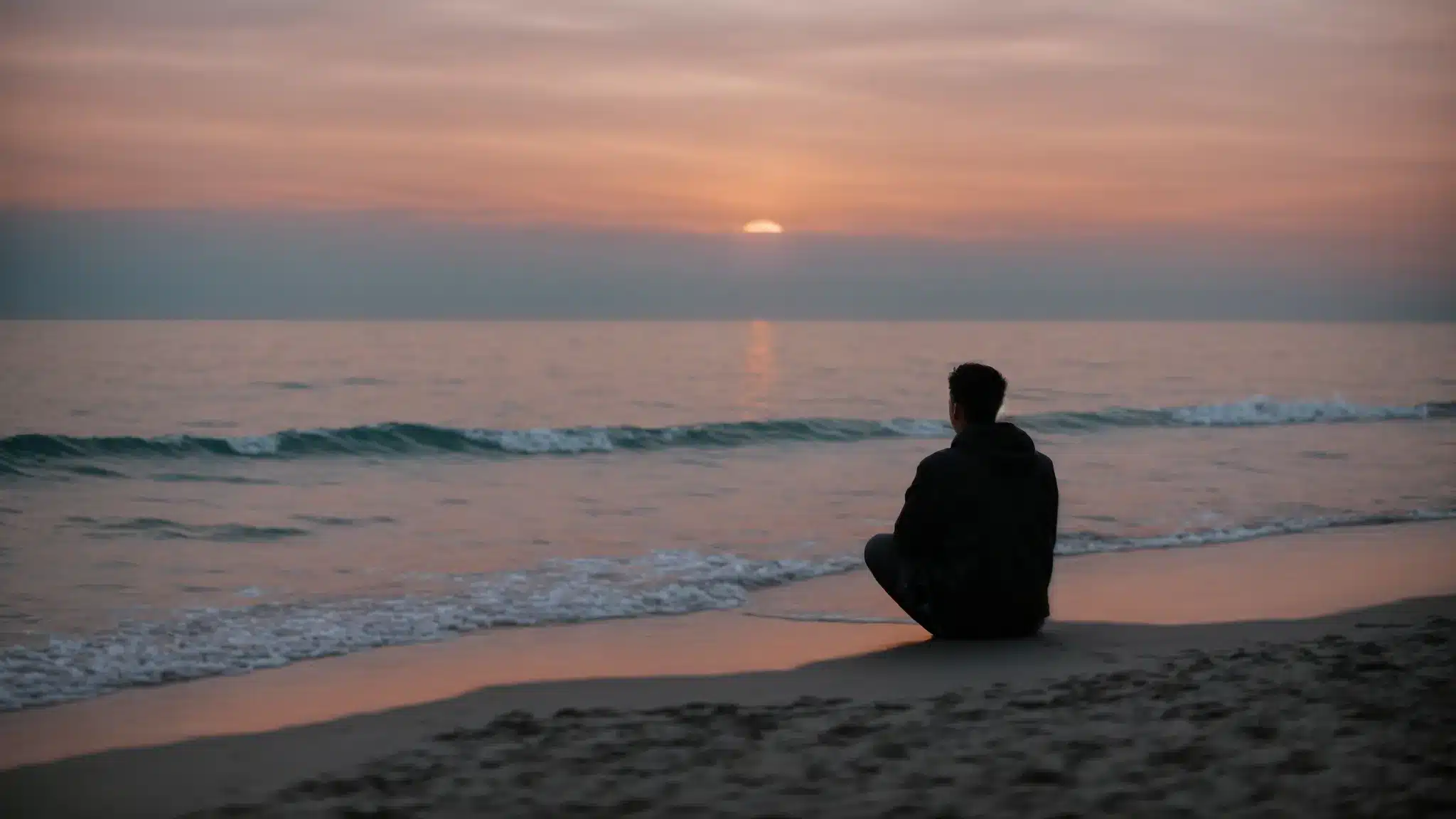 a person sitting alone on a beach at sunset, staring pensively at the sea.